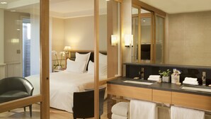 A hotel room with a bed, a desk, a chair, a large mirror, and a bathroom with a sink and towel rack. - Hôtel de L'Océan (Le Croisic)
