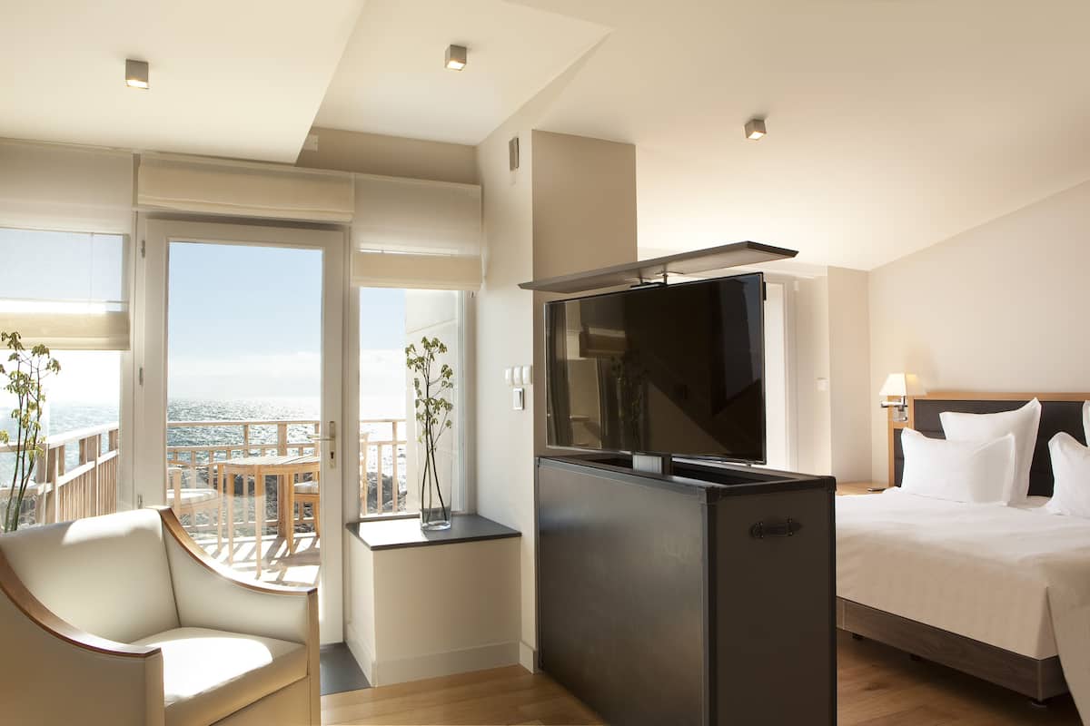 Una habitación de hotel moderna con balcón, cama, televisor y zona de estar.