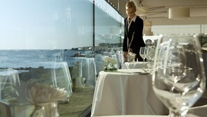 A restaurant with tables set for dining, a waiter attending to guests, and a view of the ocean. - Hôtel de L'Océan (Le Croisic)