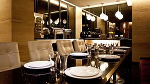 Un espace repas avec une longue table dressée pour le repas, des chaises en cuir et un éclairage moderne suspendu au plafond.