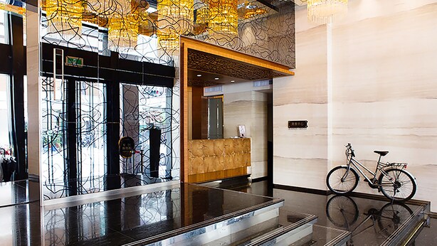 Un hall d’entrée moderne avec un ascenseur en verre, un comptoir d’accueil et un vélo garé contre le mur.