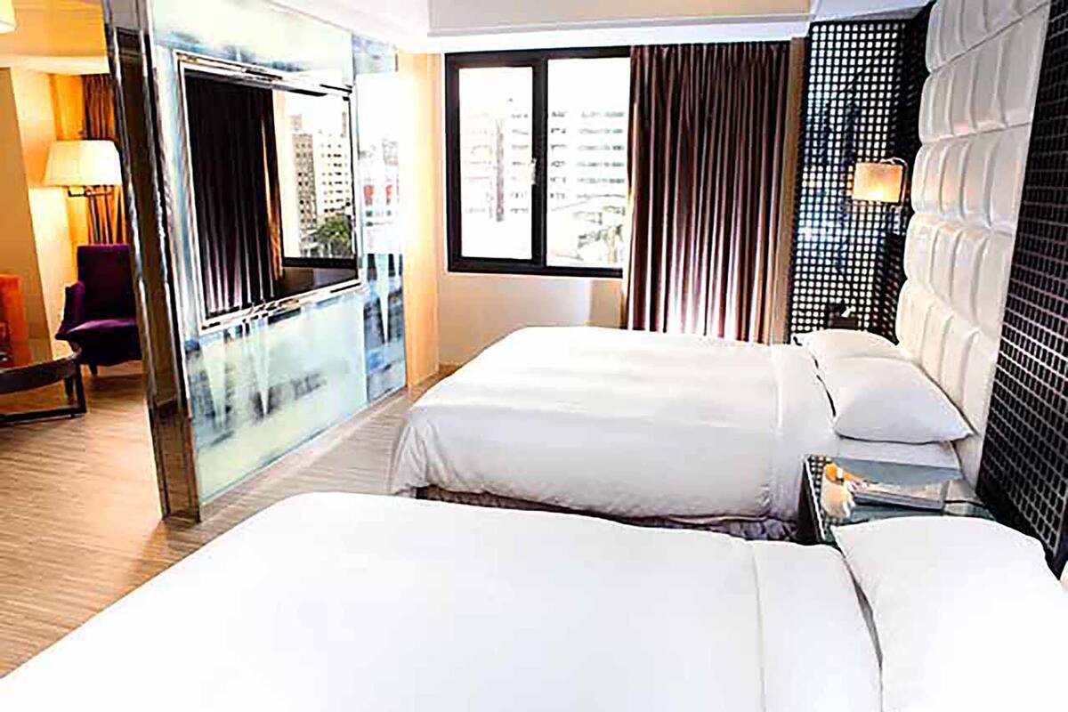 Habitación de hotel con una cama grande, un escritorio, una silla y vista a la ciudad desde la ventana.