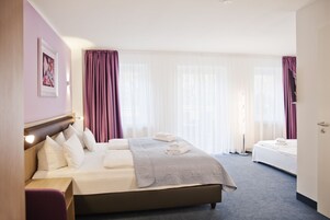 Habitación de hotel con una cama grande, una mesita de noche, una silla y una ventana con cortinas.