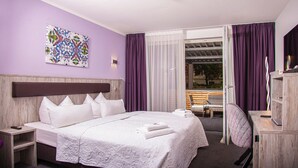 Habitación de hotel con una cama grande, cabecera de madera, escritorio, silla y vistas al exterior a través de una puerta corredera.