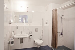 Un baño moderno con lavamanos, inodoro y zona de ducha blancos.