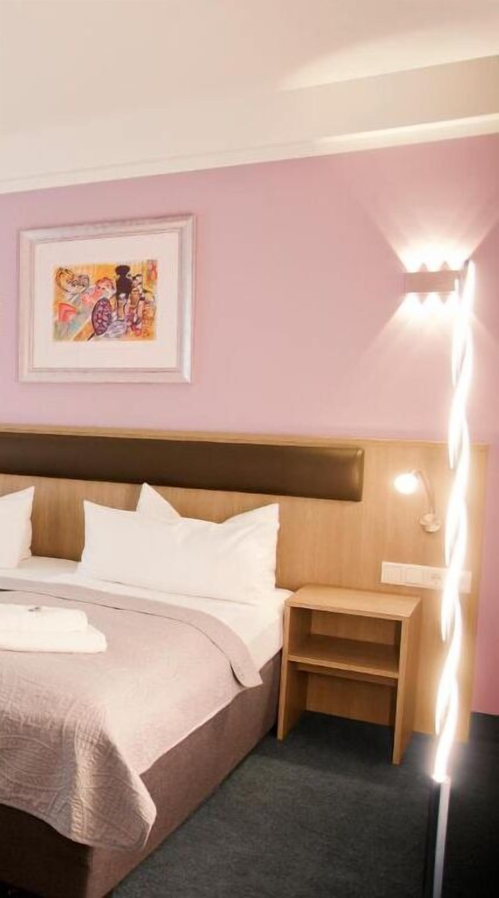 Cama bem arrumada com cabeceira, mesa de cabeceira com abajur e quadro na parede.