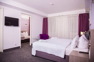 A hotel room with a large bed, a TV mounted on the wall, a desk with a lamp, and a chair.