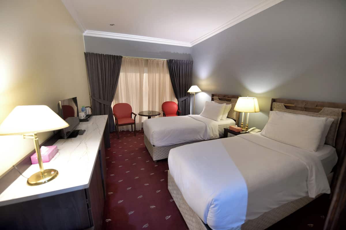 A hotel room with two beds, a desk, a chair, a small table, and a lamp.