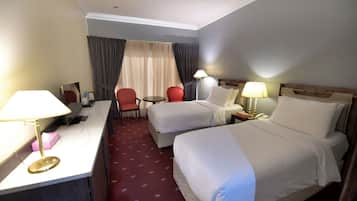 Una habitación de hotel con dos camas, un escritorio, una silla, una mesita y una lámpara.