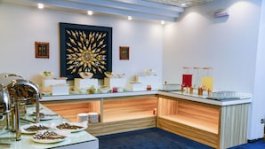 A buffet setup with various food items, serving utensils, and a decorative wall piece. - Carlton Tower Hotel Kuwait (Kuwait City)