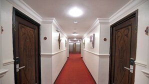 A hallway with a red carpet, wooden doors, and white walls. - Carlton Tower Hotel Kuwait (Kuwait City)