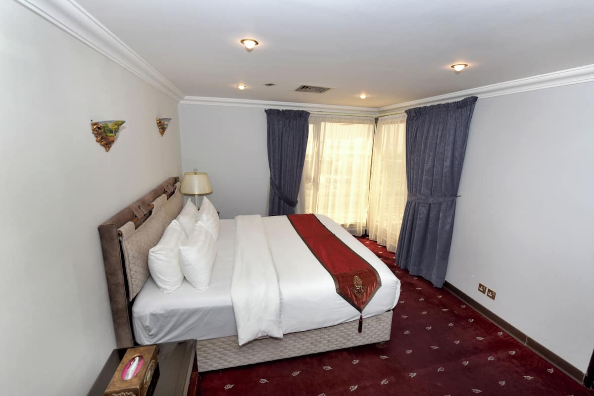 A hotel room with a large bed, a bedside table, a lamp, and a window with curtains.