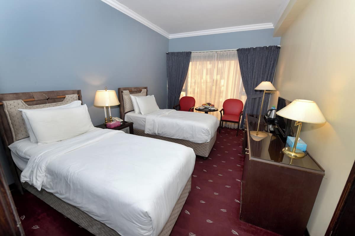 A hotel room with two beds, a desk, two chairs, a window with curtains, and a red carpet.