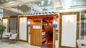 A restaurant with a wooden entrance, a sign indicating opening hours, and a seating area visible inside. - Carlton Tower Hotel Kuwait (Kuwait City)