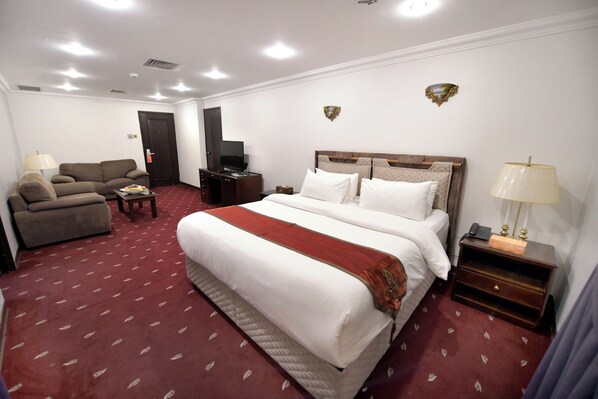A hotel room with a large bed, a sofa, a TV, and a desk. - Carlton Tower Hotel Kuwait (Kuwait City)