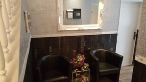 Quarto com parede de madeira escura, espelho com moldura branca, cofre e duas poltronas de couro preto.