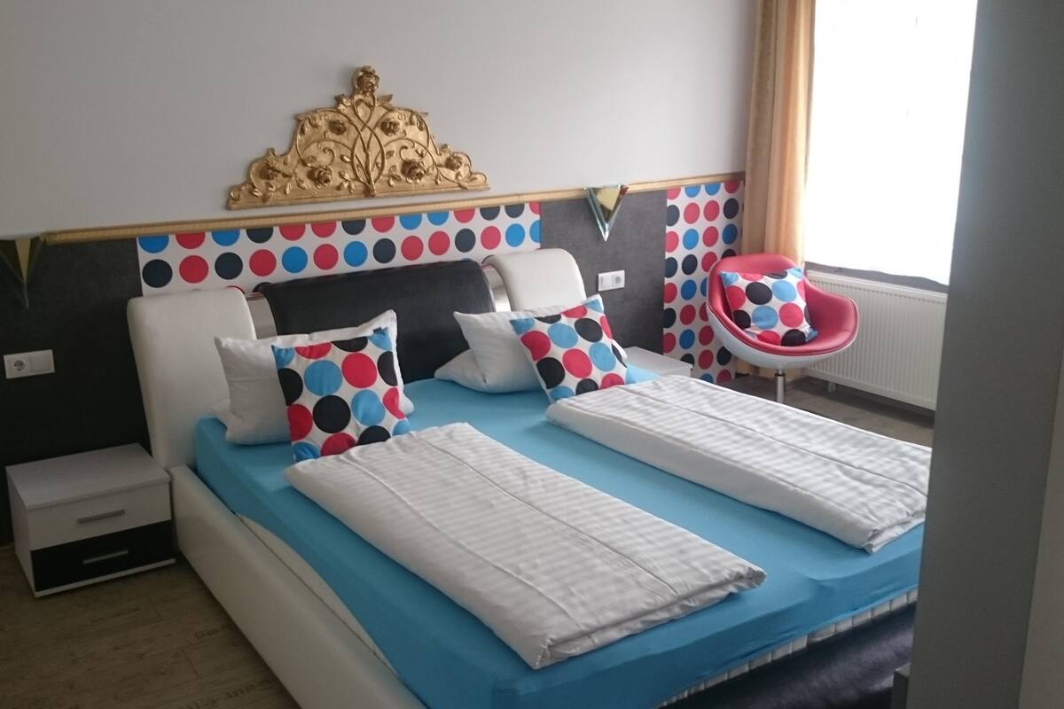 Une chambre à coucher avec un lit, deux oreillers à pois, une chaise et une tête de lit décorative.