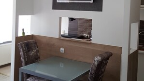 Uma área de refeições com mesa e cadeiras, uma televisão montada e um lustre decorativo.