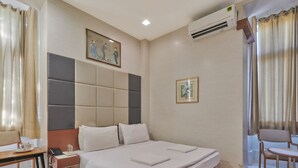 A hotel room with a large bed, bedside tables, a desk, a chair, a patterned rug, and an air conditioning unit. - Elphinstone Hotel (Mumbai)