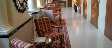 Ein Hotelkorridor mit gestreiften Sesseln, einem gemusterten Teppich und Holztüren.