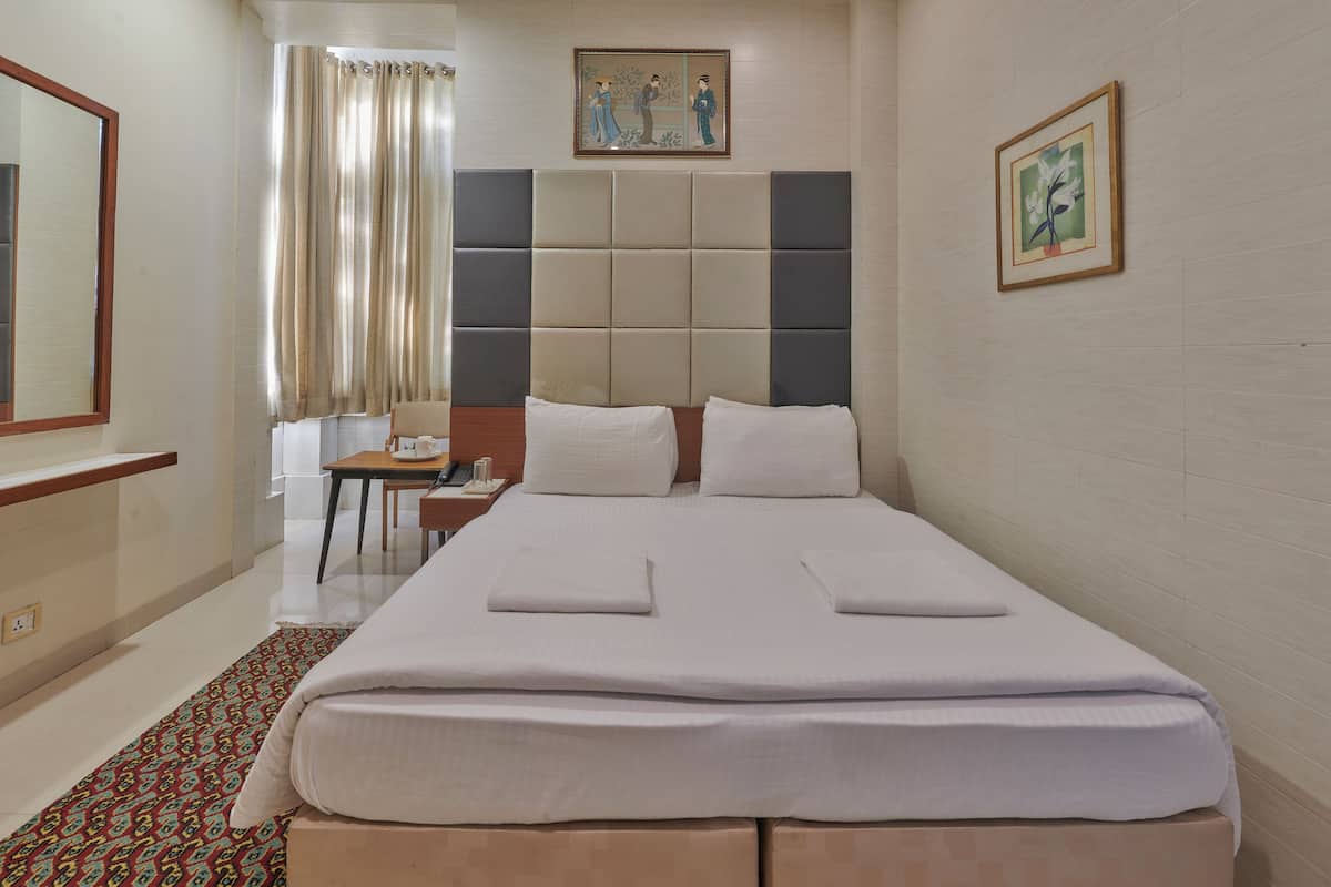 Ein Hotelzimmer mit einem großen Bett, einem Schreibtisch mit Stuhl, einem Fenster mit Vorhängen und Bildern an den Wänden.