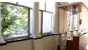 A room with large windows, a white column, a wooden counter, and a ceiling fan. - Elphinstone Hotel (Mumbai)