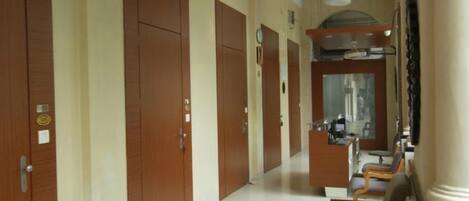 A hotel corridor with wooden doors, a reception desk, and a seating area.