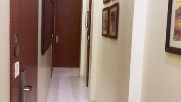 Un pasillo estrecho con una puerta de madera a la izquierda, una puerta al final y tres cuadros en la pared derecha.