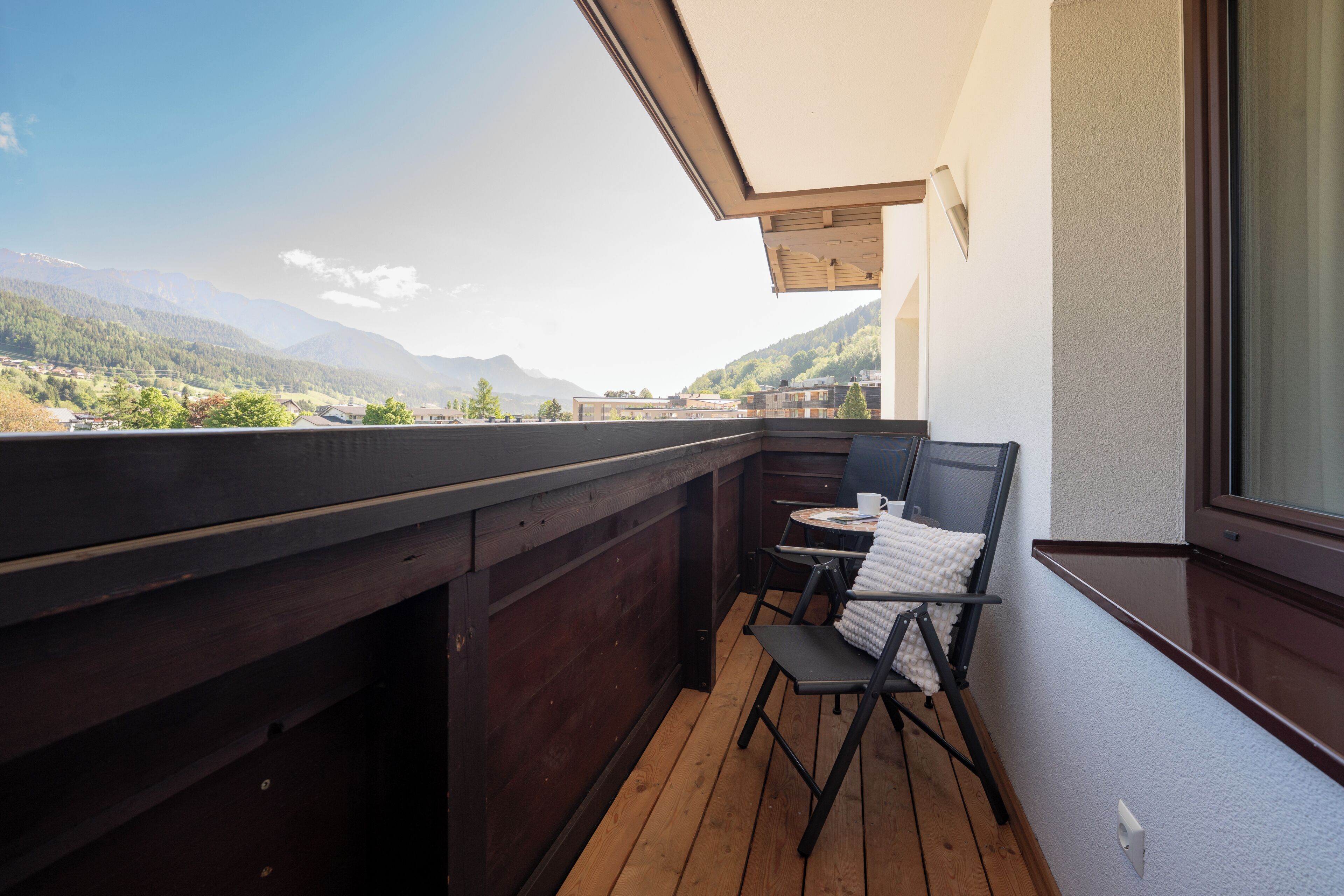A balcony with a wooden floor, a chair, a small table, and a view of mountains.