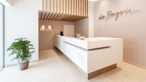 A modern reception area with a white reception desk, a potted plant, and a wall-mounted sign reading "die Bergerin". - die Bergerin - Appartements Schladming (Schladming)