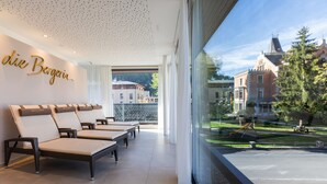 A hotel lobby with lounge chairs, a large window with a view of a courtyard and buildings, and a wall with the hotel's name. - die Bergerin - Appartements Schladming (Schladming)