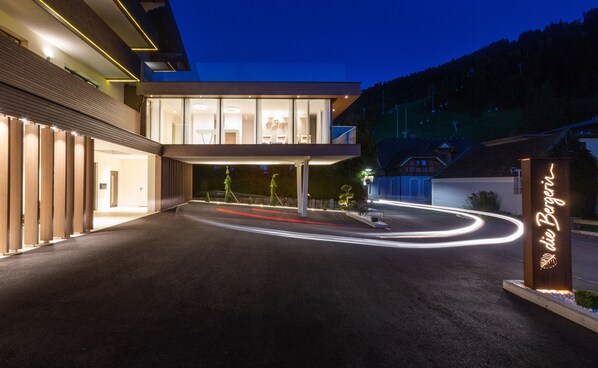 Entrada moderna de un hotel con fachada de vidrio, un camino de acceso bien iluminado y un letrero que dice "Die Bergerin".