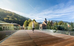 A wooden deck with a glass barrier, overlooking a mountainous landscape and a historic building with a pointed roof. - die Bergerin - Appartements Schladming (Schladming)