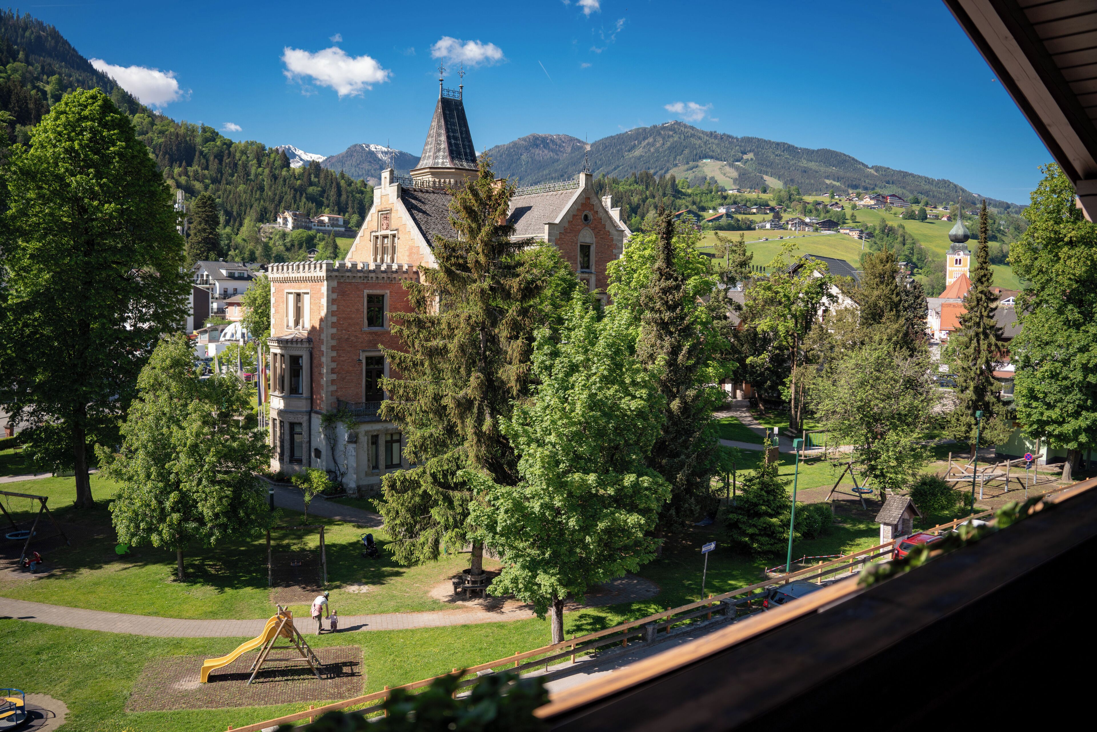 A view of a town with a prominent church, a playground, and surrounding greenery.