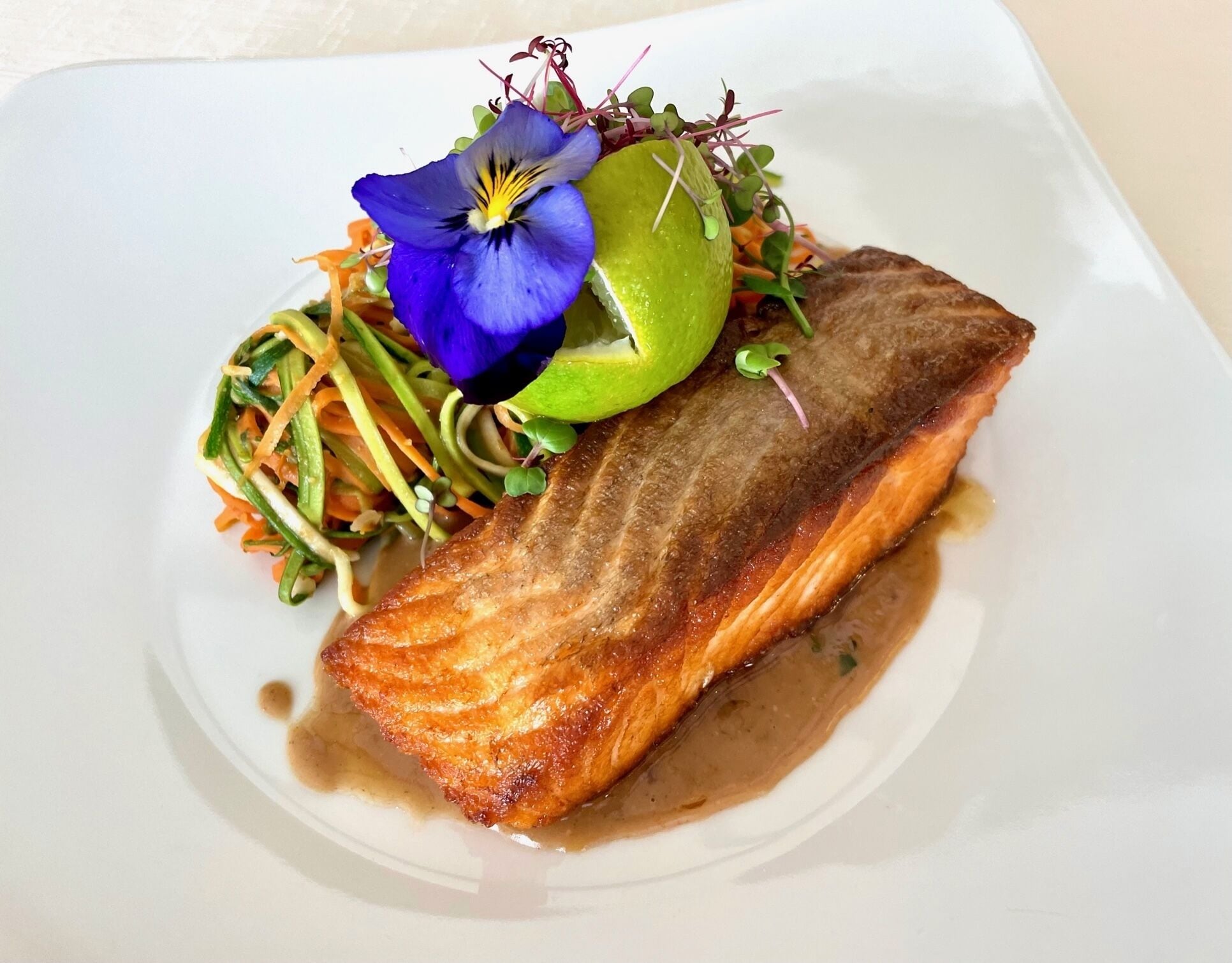 A plate with a piece of salmon, a lime, and a blue flower garnish.