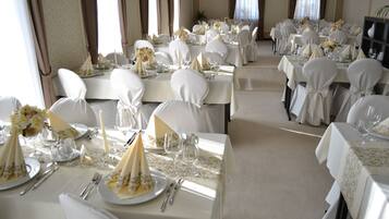 Un salón de banquetes con varias mesas dispuestas para un evento formal, destacando manteles blancos, sillas y centros de mesa con flores.