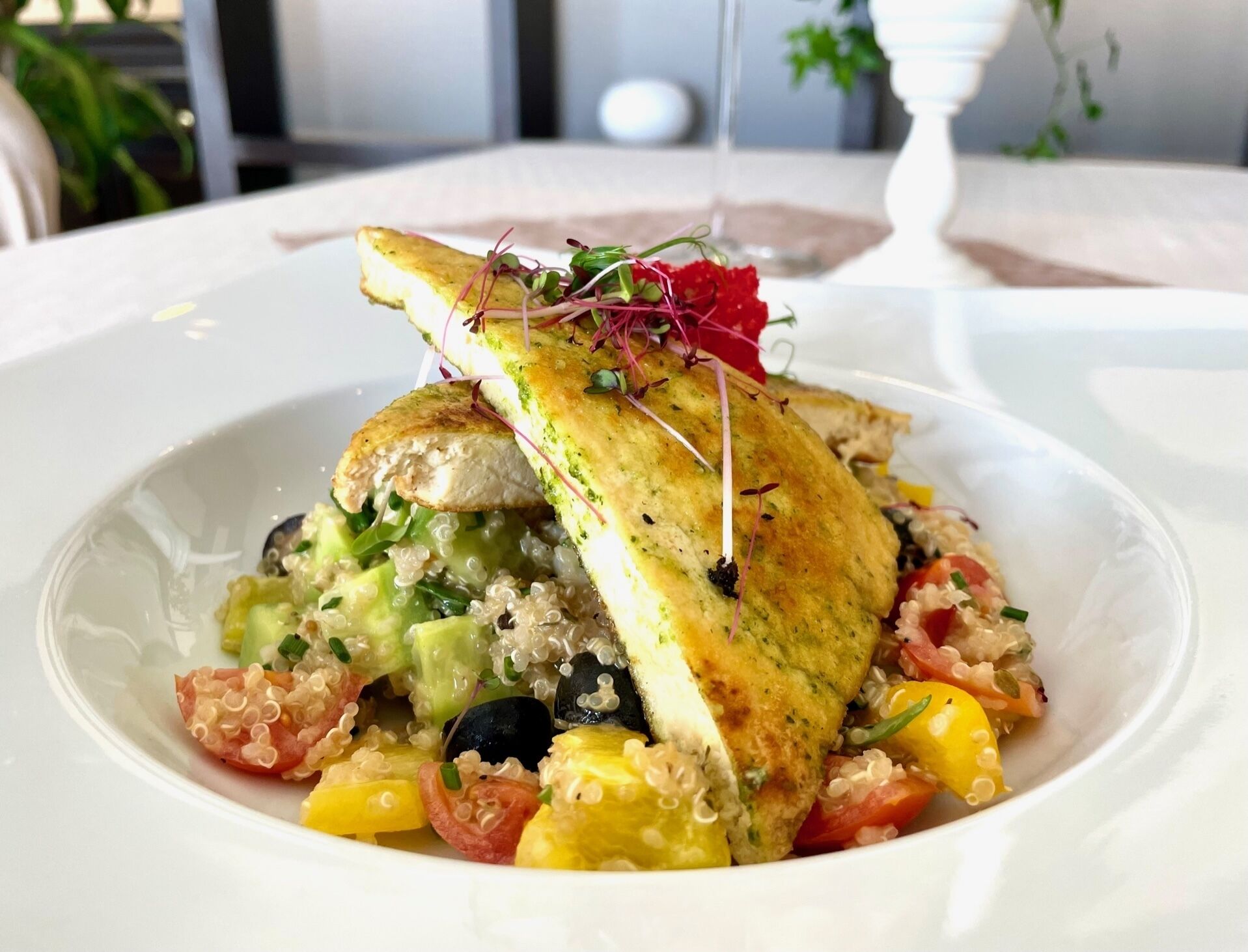 A dish with quinoa, vegetables, and a piece of grilled chicken on a white plate.