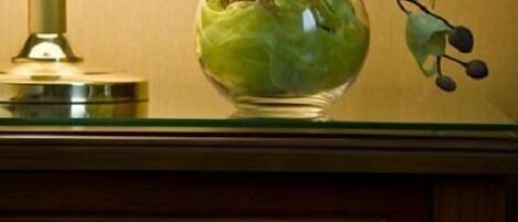 Una lámpara con pantalla color crema y un florero de vidrio con hojas verdes sobre una superficie de madera.