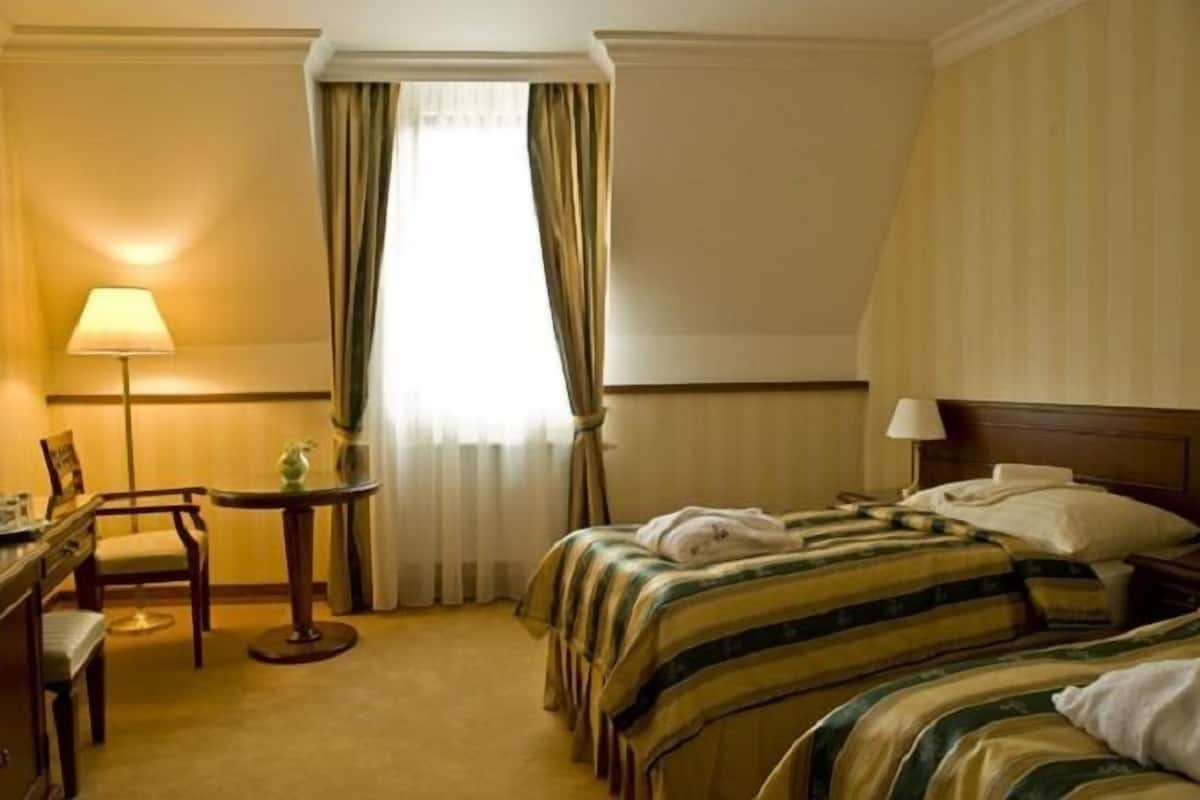 A hotel room with a bed, bedside table, lamp, chair, and a window with curtains.