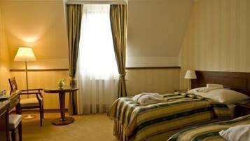 A hotel room with a bed, bedside table, lamp, chair, and a window with curtains.