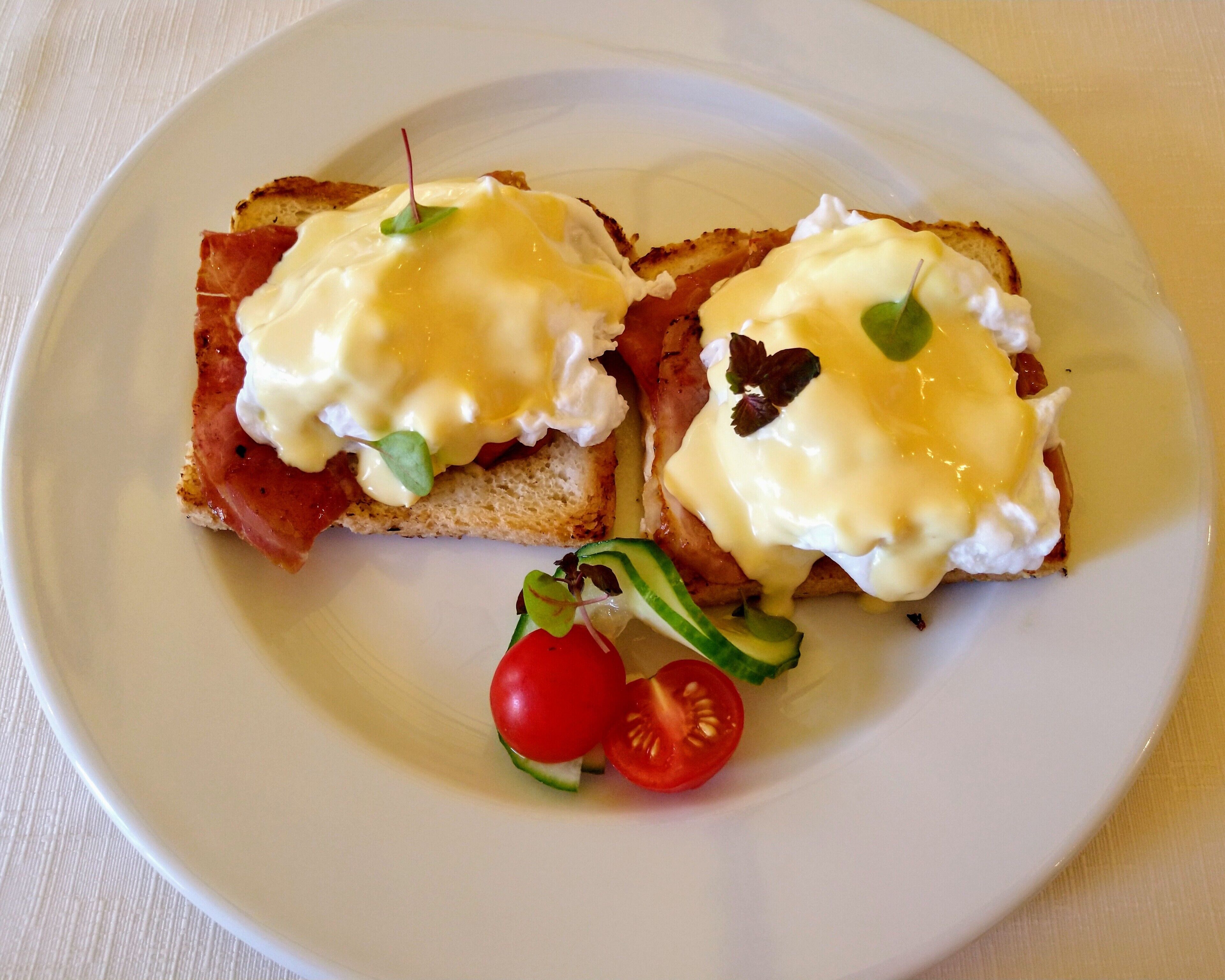 A plate with two pieces of toast topped with eggs and greens, and a side of cherry tomatoes.