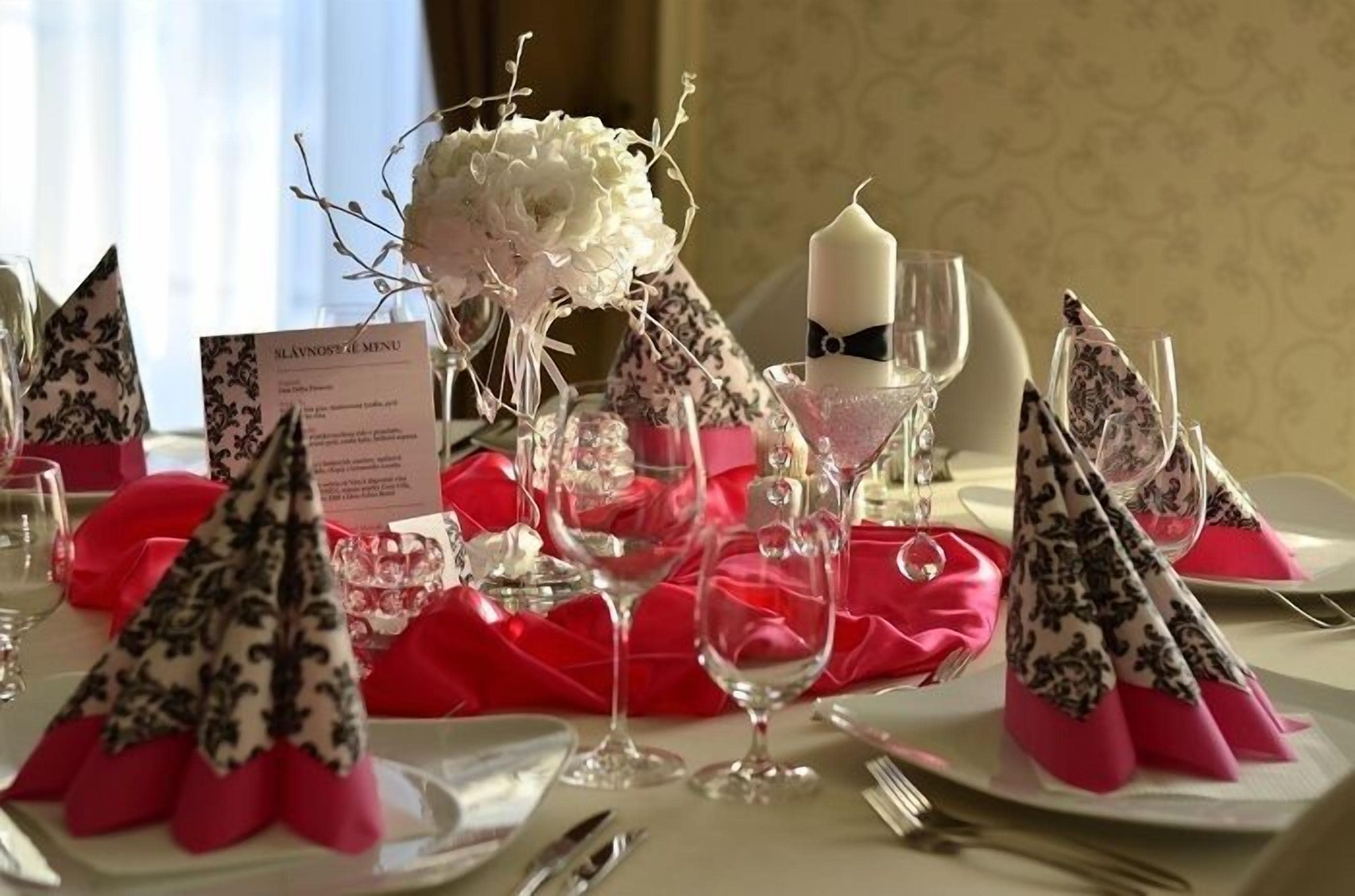 A table set with white plates, pink napkins, and clear wine glasses. A menu card is visible on the table.