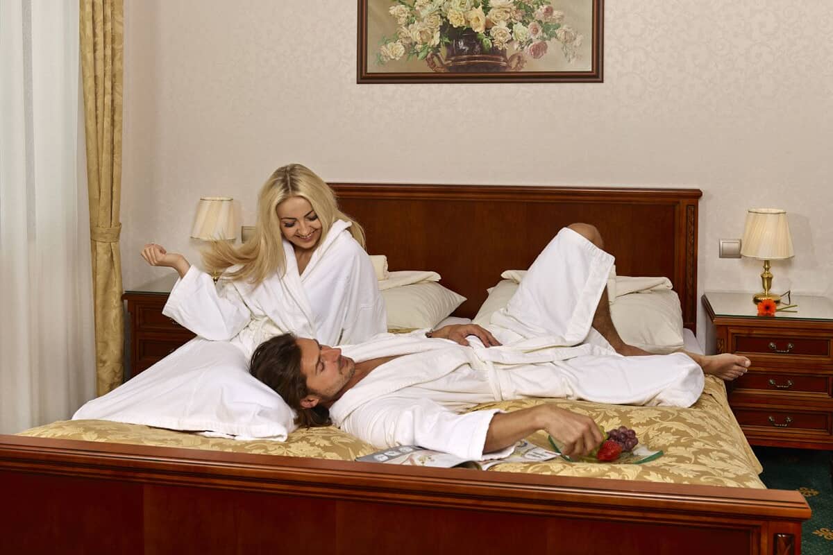 A hotel room with a wooden bed, two bedside tables with lamps, and a floral painting on the wall.