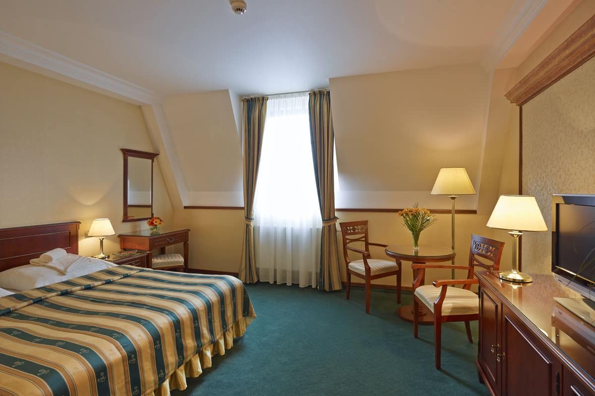 A hotel room with a bed, a desk, a chair, a television, and a window with curtains.