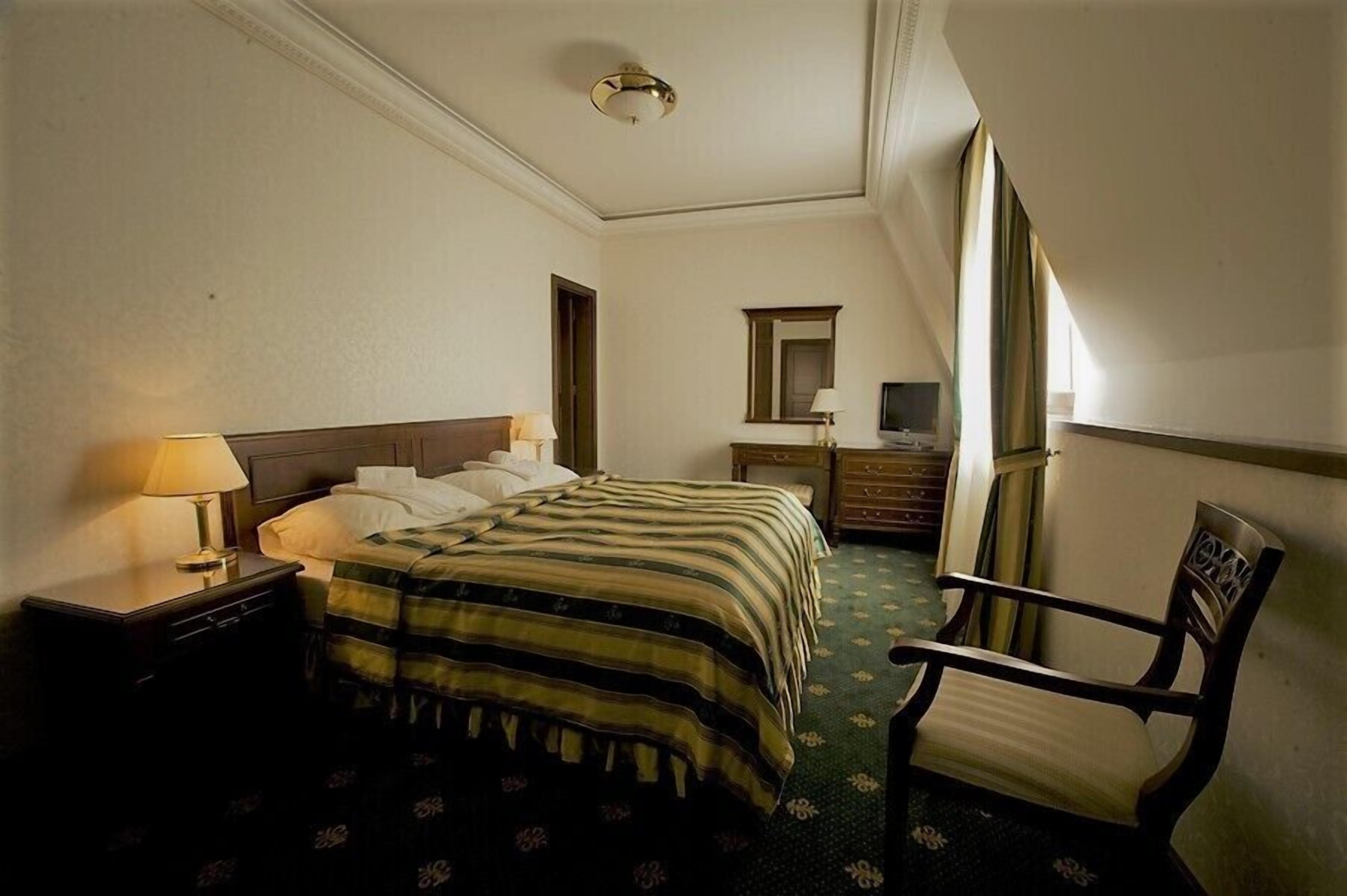 A hotel room with a bed, a chair, a dresser, and a mirror.