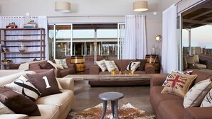Un salon spacieux avec plusieurs canapés, une table basse et une cheminée. Il y a une grande fenêtre avec des rideaux, une bibliothèque et une vue sur l’extérieur.