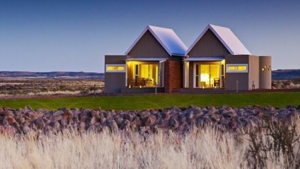 Une maison moderne composée de deux parties distinctes, chacune dotée d’un toit en pente et de grandes fenêtres, qui se dresse sur un vaste paysage ouvert.