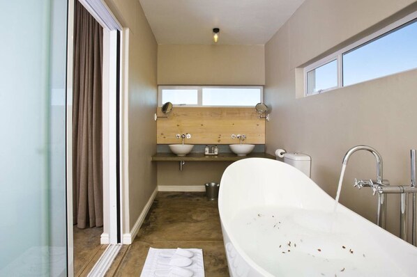 Un baño moderno con una bañera independiente, un tocador de madera con dos lavamanos y un amplio ventanal que proporciona luz natural.