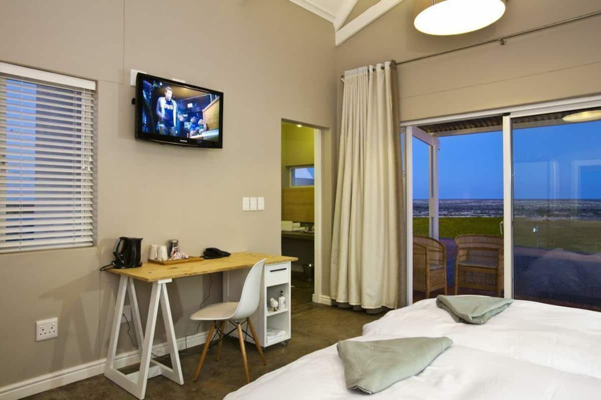 Un dormitorio con cama, escritorio, silla, televisor y vistas al exterior.