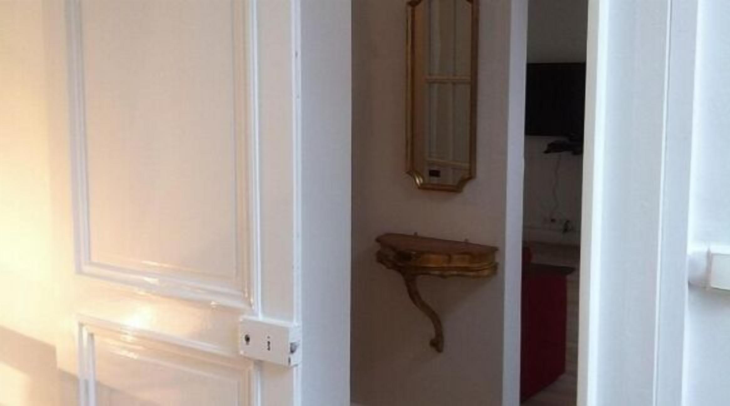 A white door with a wall-mounted shelf and a framed mirror above it.
